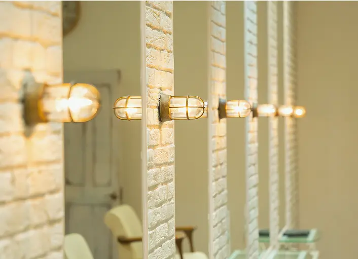 美容室の白いレンガ調の壁に並んだ温かみのある照明ランプ