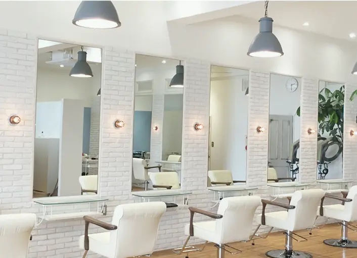 白いレンガ調の壁に鏡とセット椅子が並ぶ明るい美容室のセット面